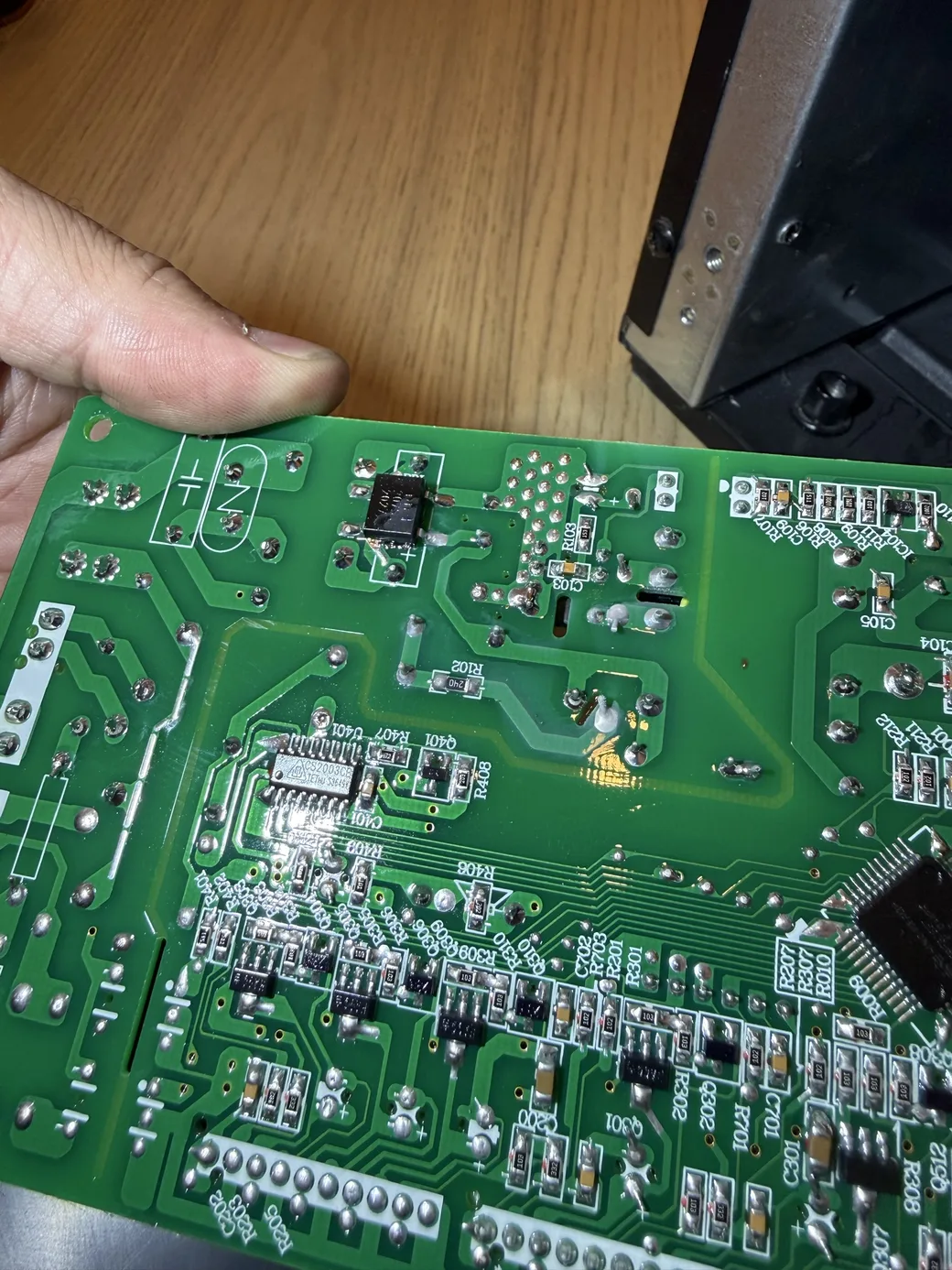 A hand holding the solder side of a green appliance circuit board